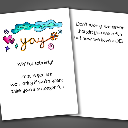 Funny sobriety card with the word yay, hearts and a cheerful scene drawn on the front of the card. Inside the card is a funny joke that says at least we all have a DD now!